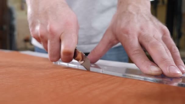 Mains de l'artisan du cuir habile en utilisant un motif en plastique et un couteau en cuir pour découper une partie d'un morceau de cuir rouge, gros plan. Couteau industriel homme coupe la pièce à usiner de la peau. Images de 4 k
 - Séquence, vidéo