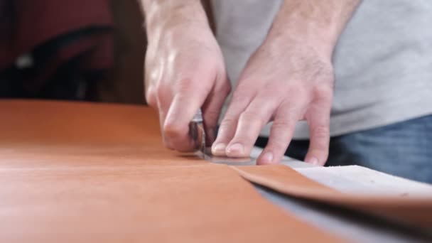 Mains de l'artisan du cuir habile en utilisant un motif en plastique et un couteau en cuir pour découper une partie d'un morceau de cuir rouge, gros plan. Couteau industriel homme coupe la pièce à usiner de la peau. Images de 4 k
 - Séquence, vidéo