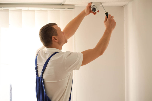Technician installing CCTV camera on ceiling indoors - Fotoğraf, Görsel