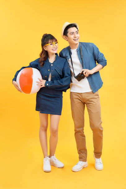 Playful Asian couple in summer casual clothes with beach accessories studio shot isolated on yellow background - Photo, Image