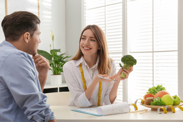 Young nutritionist consulting patient at table in clinic - Φωτογραφία, εικόνα