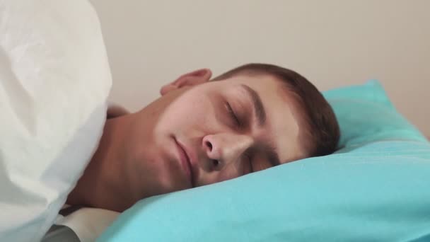 falls asleep young man close-up on a soft pillow. selective focus, comfortable bed, healthy sleep - Video, Çekim