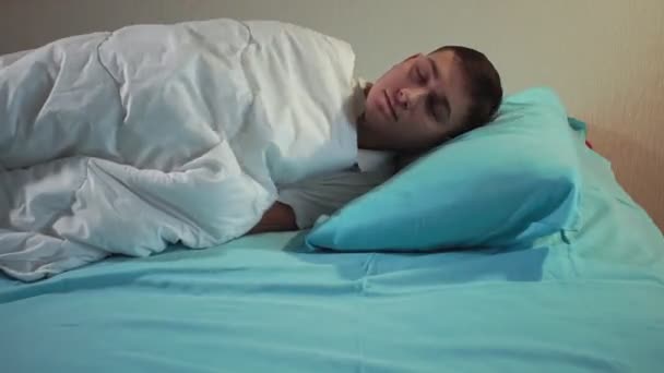 young man goes to bed with the light on in a cozy bed. Restful sleep - 映像、動画