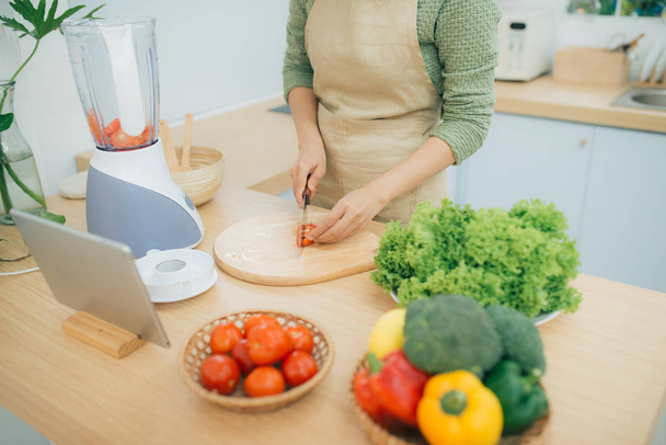 Bild einer jungen Frau, die mit Tablet-Computer in der Küche steht und Gemüsesalat kocht - Foto, Bild