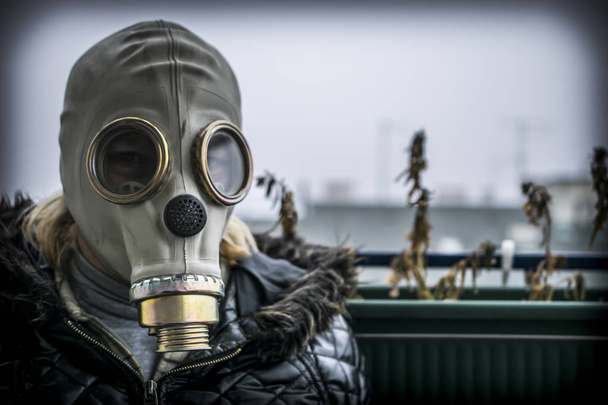 Une femme d'âge moyen avec un masque à gaz avec du brouillard et de la pollution en arrière-plan
 - Photo, image