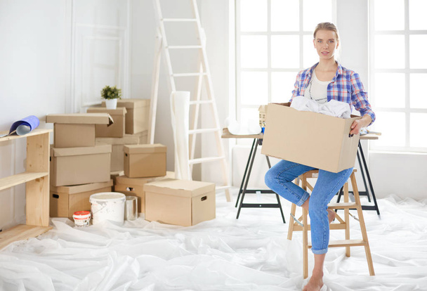 A beautiful single young woman unpacking boxes and moving into a new home - Фото, изображение