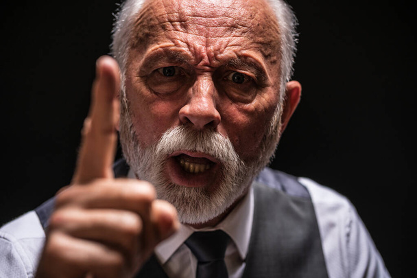 Egy dühös öregember portréja, aki fenyegetőzik. Fekete háttér. - Fotó, kép