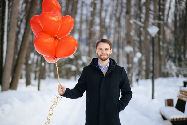 young man in coat with red air balloons outdoors - Photo, image