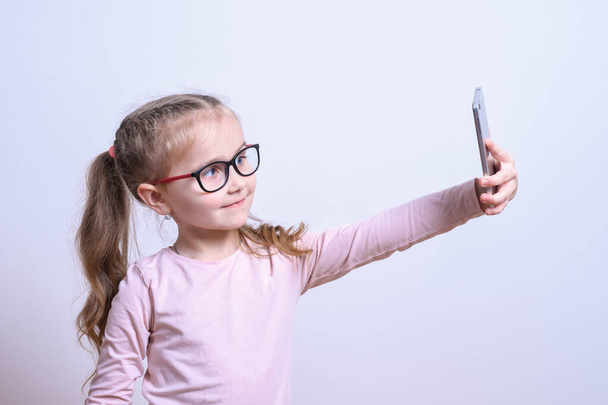 Portret małej białej dziewczynki zrobić selfie na telefon komórkowy na szarym tle - Zdjęcie, obraz