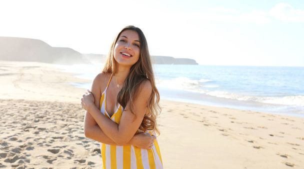Girato di una bella donna brasiliana che si abbraccia in piedi su una spiaggia in abito estivo
 - Foto, immagini