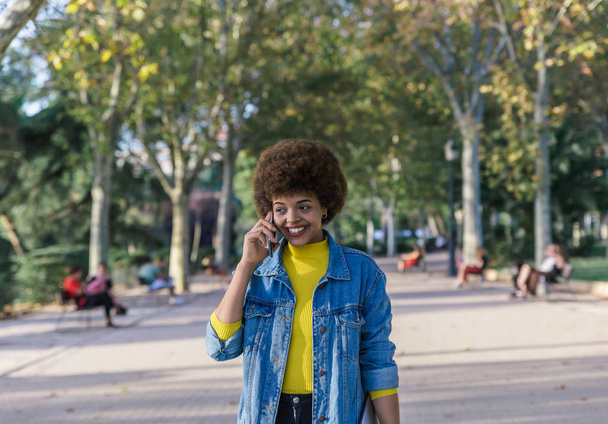 Beautiful brunette girl with afro hair smiles with her perfect white teeth while talking on her mobile phone - Fotó, kép