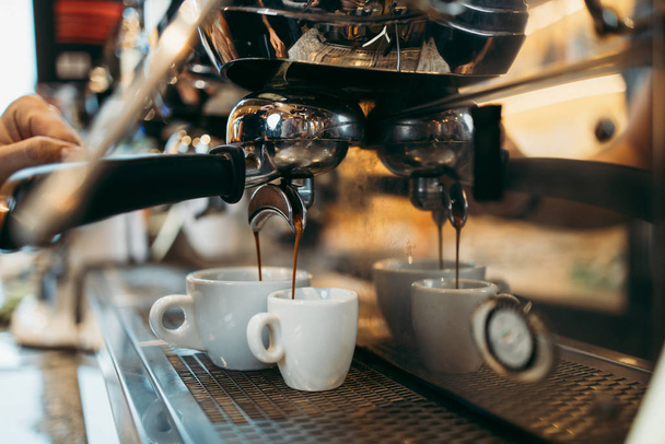 Close up shot of experienced barman or bartender hands making delicious and fresh espresso coffee drink on machine. - 写真・画像