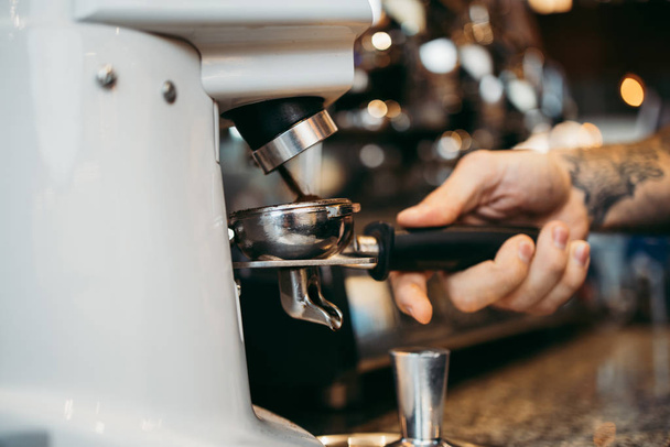 Close up shot of professional bartender preparing espresso coffee in exclusive cafe bar or cafeteria. He using coffee mill or grinder. - Foto, Bild