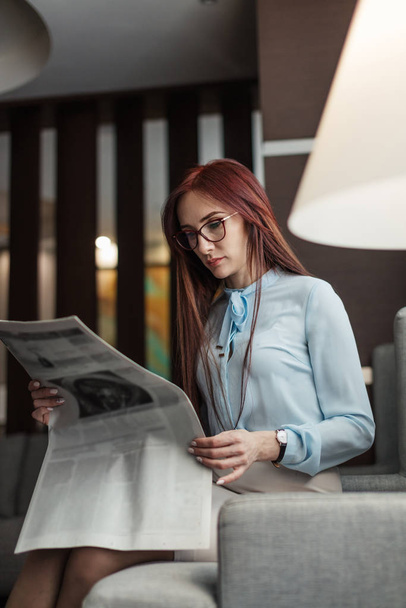 Happy young businesswoman reading newspaper in hotel lobby - Photo, Image