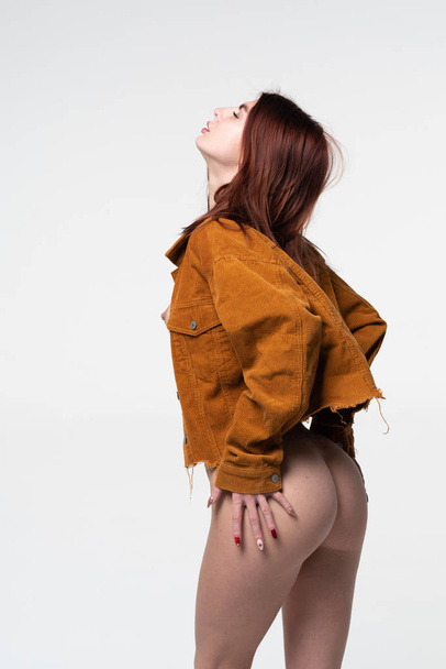 young beautiful girl is standing in a brown jacket in the studio near the white wall - Photo, Image