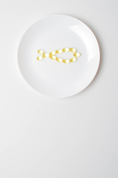 Omega-3 polyunsaturated fatty acids on a plate. Fish oil softgels on a white plate in a shape of a fish. Meal replacement. Casual  nutrition prescription. Copy space below. - Foto, afbeelding