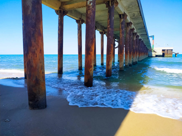 View under the dock at the beach. Coming and foamy waves - Photo, Image