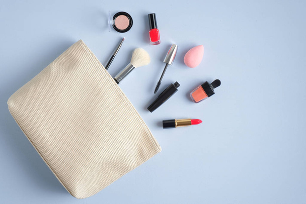 Make-up cosmetic bag on blue background. Stylish makeup artist pouch with beauty products. Flat lay, top view - Photo, Image