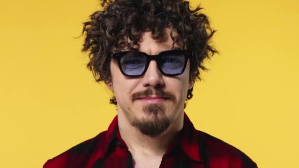 Amazed and happy european man in blue sunglasses smiling. Handsome guy with stylish curly hair isolated on yellow background. Lifestyle concept. - Filmagem, Vídeo