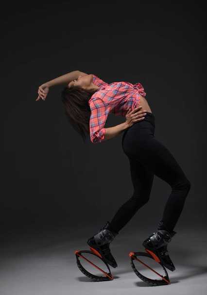 Young and pretty fitness instructor makes exercise using jumping boots. - Photo, image