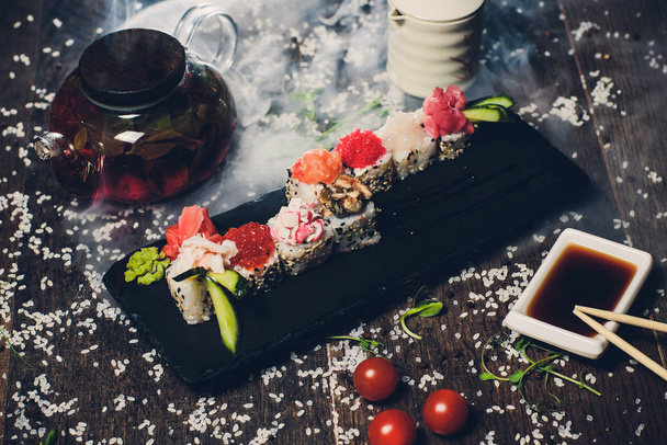 various sushi on white plate with chopsticks on wooden background. - Foto, afbeelding