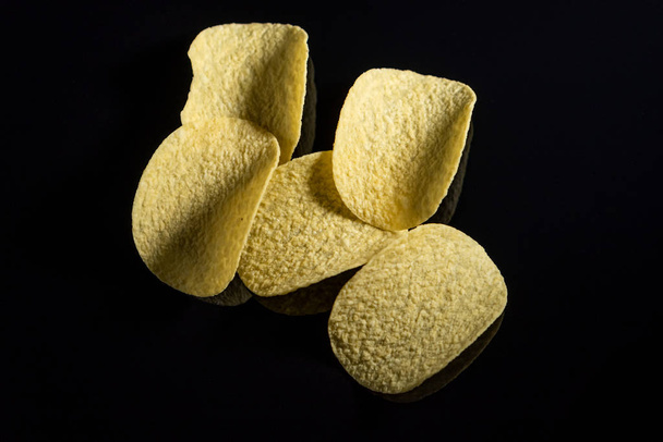 Chipsy ziemniaczane na czarnym szklanym tle. Zbliżenie, widok z góry - Zdjęcie, obraz