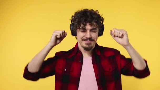 Handsome happy european man with beard in red shirt smiling and dancing isolated on yellow background. Guy in headphones listening to music. Lifestyle concept. Slow motion. - Video, Çekim