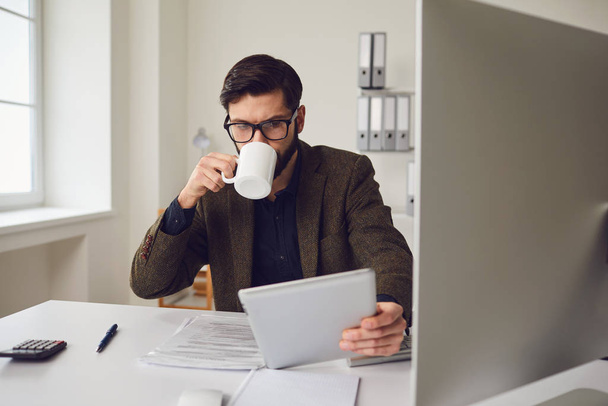 Businessman worker drinking a coffee mug while sitting at a table with a computer working in the office. - Foto, imagen