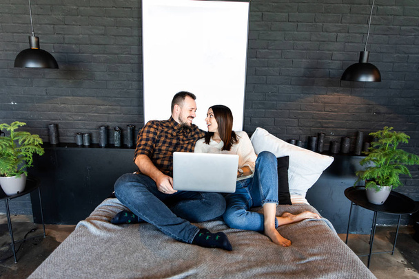 Couple with laptop in casual clothes on bed. - Fotoğraf, Görsel