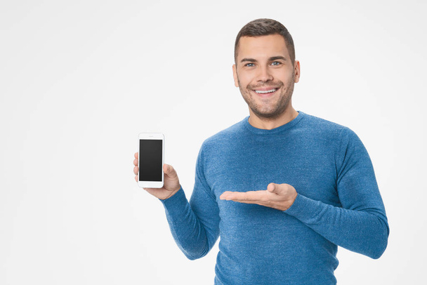 Shot of man in blue sweater presenting smart phone with black screen with copyspace isolated on white background - Photo, image