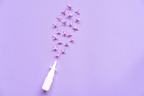 weiße Nasenspraydose auf violettem Hintergrund, Kochsalzlösung zur Behandlung von Nasenstauungen und Allergien, flache Lage, gesundes Konzept, Fliederblüten - Foto, Bild