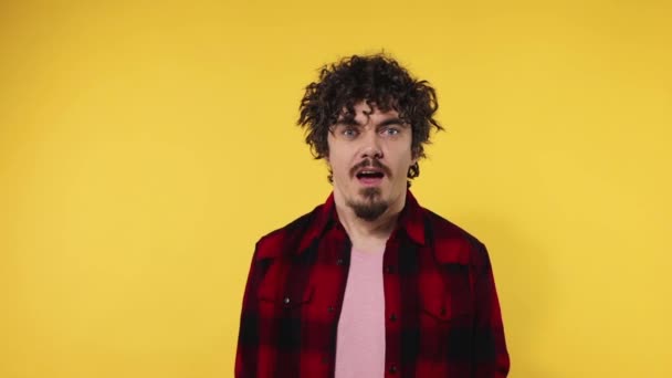 Man celebrates team victory. Closeup portrait of happy smiling guy with curly hair looking at camera isolated on yellow background. Slow motion. - Materiał filmowy, wideo