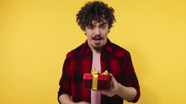 A man gives a red gift for Valentines Day lovers or International Womens Day. Birthday surprise. Handsome happy european man with beard in shirt smiling isolated on yellow background. Slow motion. - Filmagem, Vídeo