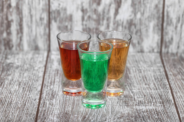 Drei Schüsse mit verschiedenen alkoholischen Getränken stehen auf einem Holztisch - Foto, Bild