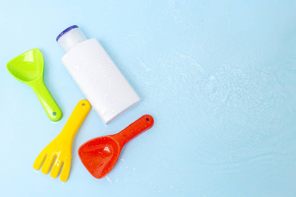 Sonnencreme SPF-Lotion, um Kinderhaut von der Sonne mit bunten Wasserspielzeug auf blauer Wasseroberfläche des Pools, Draufsicht zu beheben. Konzept UV-Schutzprodukt, Sommer-Kinderkosmetik. - Foto, Bild