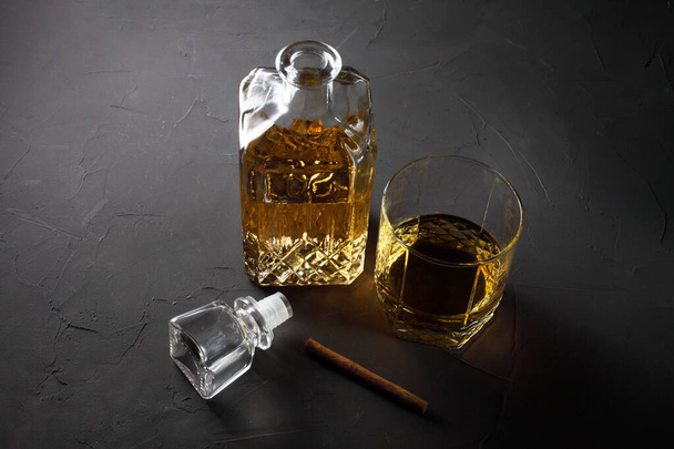 un rum in un decanter e un bicchiere nelle vicinanze giace un sigaro su uno sfondo scuro
 - Foto, immagini