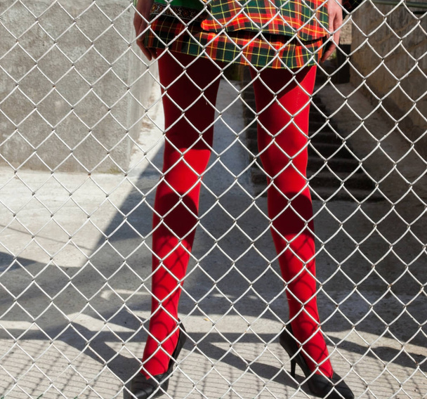 Woman's legs in red tights behind the metal mesh fence - Foto, Bild