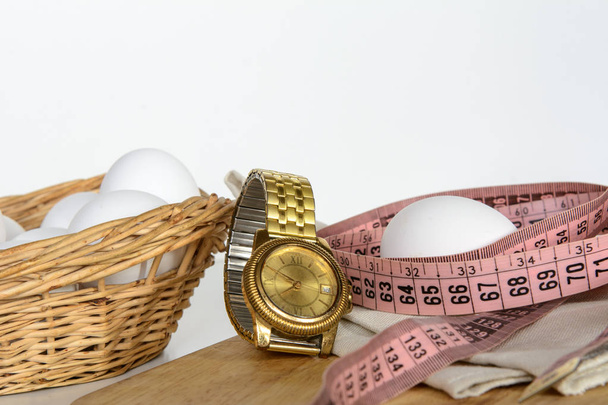 Jajka są w koszyku. Jajo leży oddzielnie na elastycznym mierniku i na serwetce. Pomiędzy nimi jest zegarek. Koncepcja - schudnąć, dieta białkowa, zgodnie z ruchem wskazówek zegara - Zdjęcie, obraz