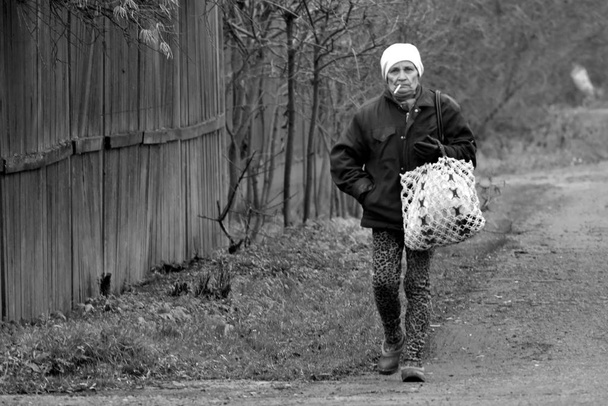 Monochrome photo. Old woman is walking with an outdoor cigarette. Pensioner woman - Fotoğraf, Görsel