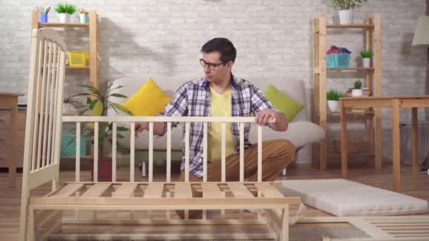 positive young man future father collects a childs bed in the bedroom - Metraje, vídeo