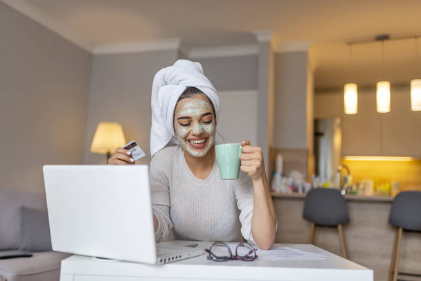 Woman with cosmetic face mask shopping online from her home. Leisure time at home. pPortrait of beautiful woman with facial taking a coffee at home while use internet with modern laptop computer  - Fotoğraf, Görsel