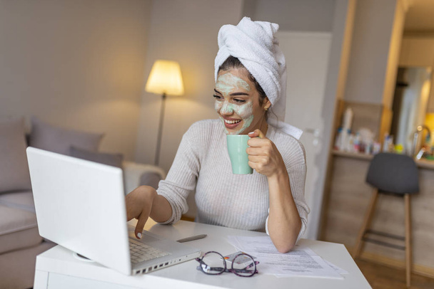 Woman wearing facial mask enjoying at home and using her laptop. Multitasking young woman with beauty treatment facial mask chatting using laptop at home.  - Foto, Imagen