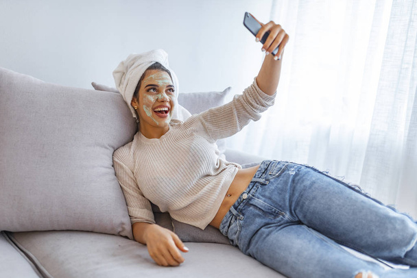Girl with beauty mask relaxing at home, messaging text on cell phone. Young woman texting message on smartphone, mobile telephone. Female beauty, skin and body care. - Fotoğraf, Görsel