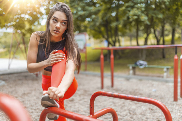 Young female workout before fitness training session at the park. Healthy young woman warming up outdoors. She is stretching her legs and looking away,hi key. - Foto, immagini