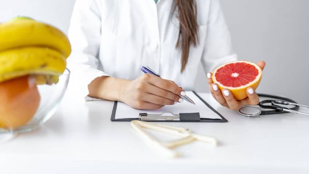 Nutritionist writing diet plan for patient, panorama, copy space. Female nutritionist with fruits working at her desk. Dietitian working on diet plan. Weight loss and right nutrition concept - Foto, Imagen