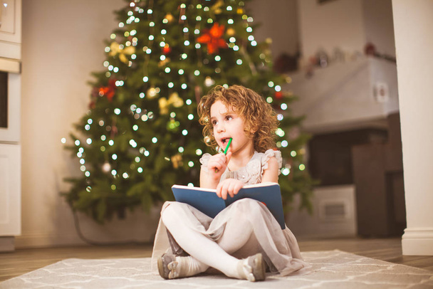 Fille rêveuse assise près de l'arbre de Noël décoré
 - Photo, image