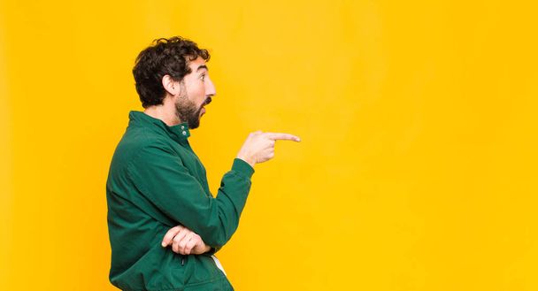 young crazy bearded man against orange wall copy space. - Фото, изображение