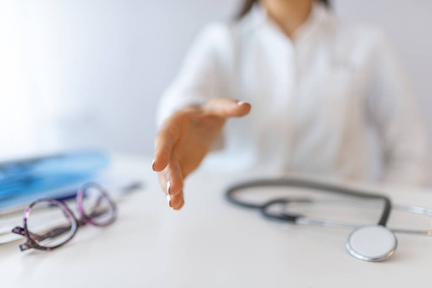 Female medicine doctor offering hand to shake closeup. Greeting and welcoming gesture. Medical cure and tests advertisement concept. Physician ready to examine patient. Focus on hand - Foto, imagen