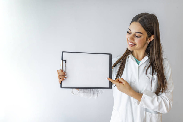 Medical sign. Young woman doctor / nurse showing empty blank clipboard sign with copy space for text. Caucasian female model isolated over white background. - Fotografie, Obrázek
