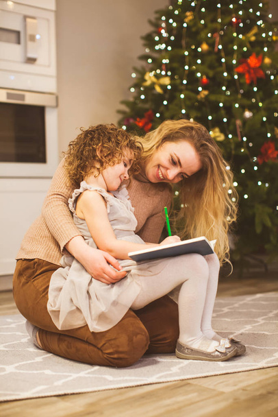 Mother holding her daughter on knees near Christmas tree - Foto, immagini